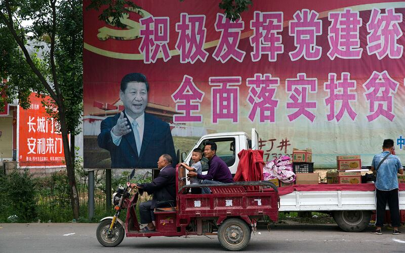 河南省平顶山市居民经过习近平的海报和“积极发挥党的建设引领作用,全面实施脱贫攻坚计划”的部分标语。(美联社)