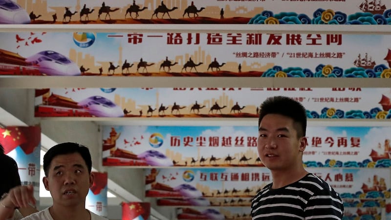 两名中国男子站在“一带一路”的宣传标语前。(美联社)