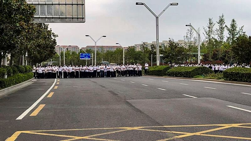 Plainclothes security officers stand on the road as people stage a protest at the entrance to a branch of China's central bank in Zhengzhou in central China's Henan Province on July 10, 2022. Credit: AP