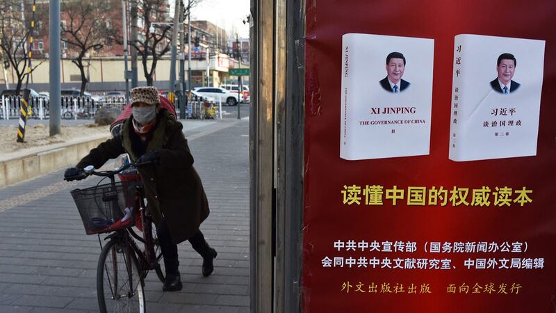 2018年1月19日,北京市一名妇女骑车经过海报,宣传有关习近平的书。 (法新社)