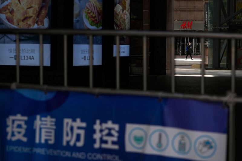 2022 年 5 月 12 日,在北京朝阳区,当局下令关闭非必要业务并要求人们在家工作后,一名戴着口罩的妇女走过关闭的商场。(美联社)