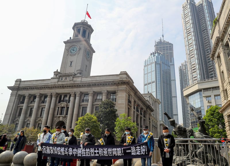 图为,2020年4月4日,武汉市江汉关大楼钟声十点鸣钟降半旗,市民拉出横幅追忆逝者。(路透社)